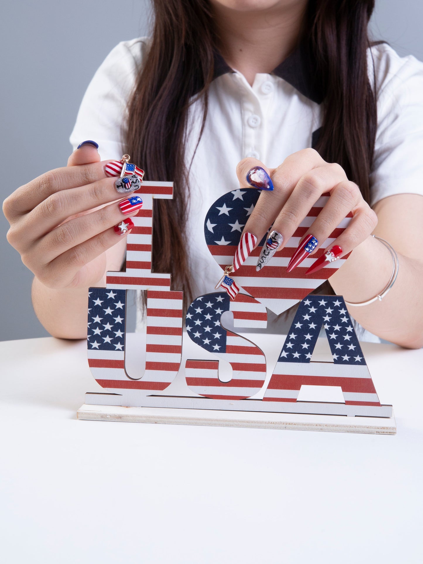 Person with American flag-themed press-on nails holding 'I a???¡ì?¡ì USA' decor. Patriotic red, white, and blue nail design perfect for Independence Day celebrations and July 4th parties.